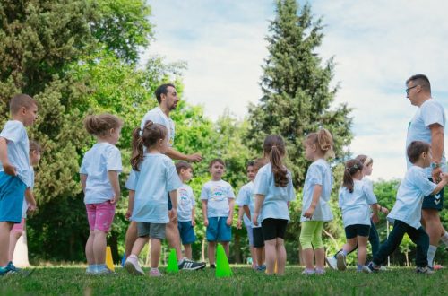 Group of children and teachers playing and learning in a sunny park setting.