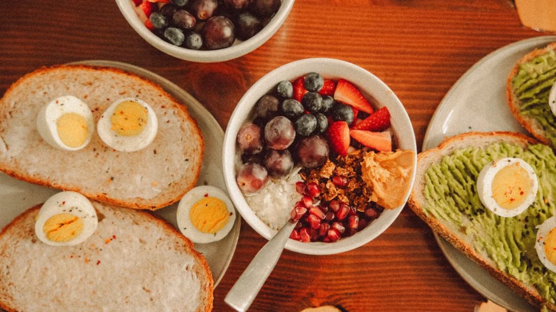 A fresh and vibrant breakfast flat lay featuring a yogurt bowl with fruits and toast with eggs and avocado.
