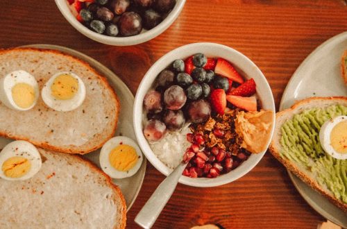 A fresh and vibrant breakfast flat lay featuring a yogurt bowl with fruits and toast with eggs and avocado.